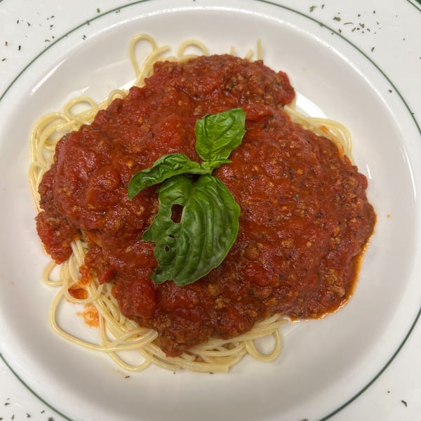 Spaghetti with a rich red meat sauce and a fresh basil leaf on a white plate with green trim.