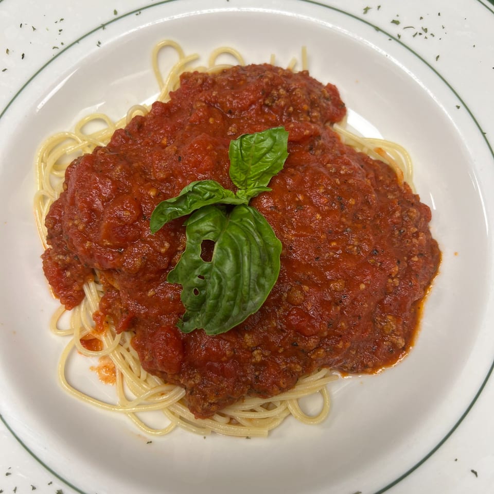 Spaghetti with a rich red meat sauce and a fresh basil leaf on a white plate with green trim.