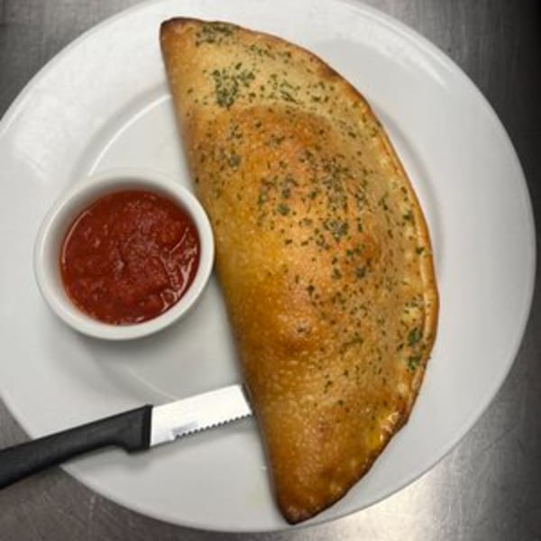 Golden-brown calzone sprinkled with herbs, served with a side of red marinara sauce and a knife.