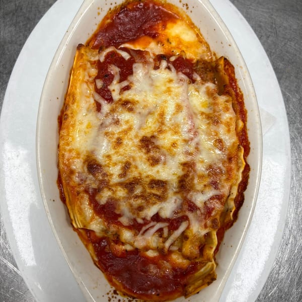 A baked lasagna with melted cheese and red sauce in a white oval dish.