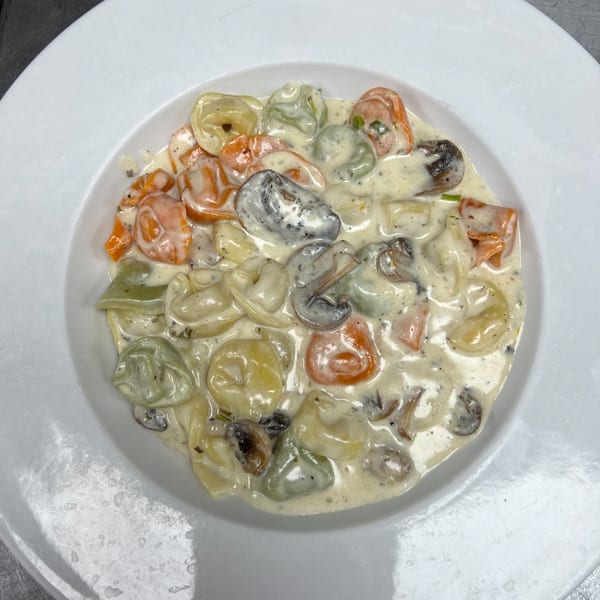Colorful tortellini pasta in a creamy white sauce with mushrooms, served in a white bowl.
