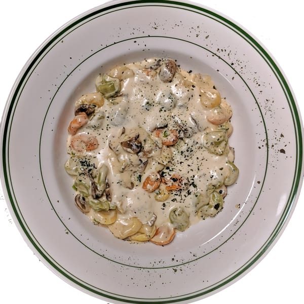 Roma Ristorante Italiano's tortellini pasta with creamy white sauce, mushrooms, and herbs in a white bowl.