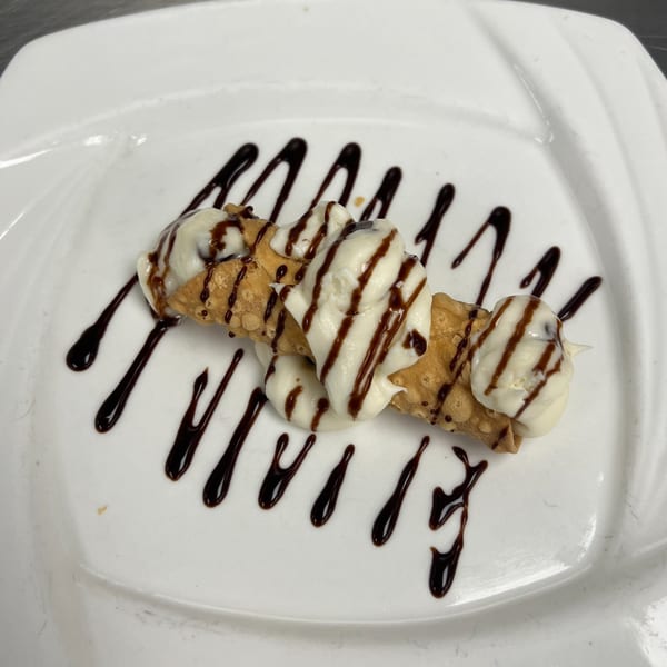 A cannoli from Roma Ristorante Italiano, drizzled with chocolate sauce and filled with creamy white ricotta.