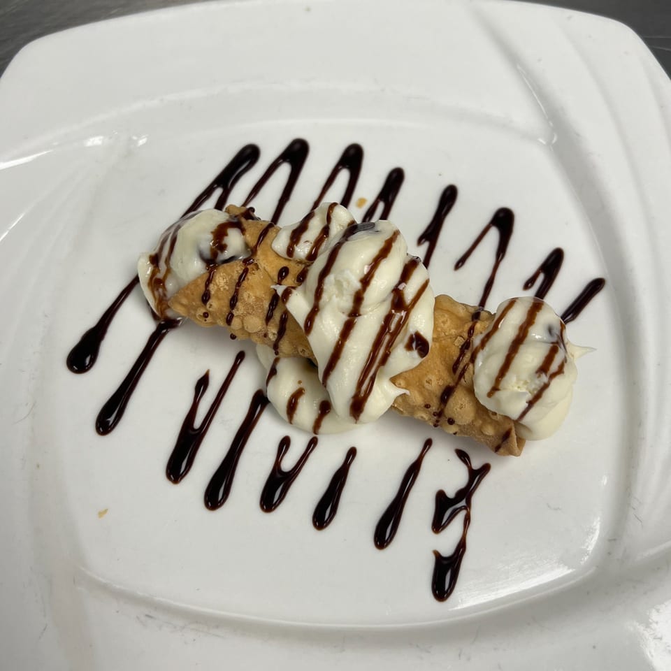 A cannoli from Roma Ristorante Italiano, drizzled with chocolate sauce and filled with creamy white ricotta.