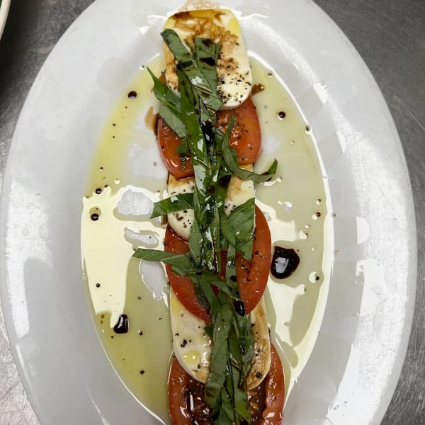 Caprese salad with sliced tomatoes, mozzarella, fresh basil, olive oil, and balsamic glaze.