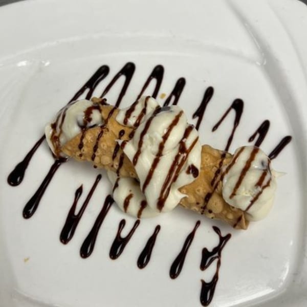 A cannoli dessert from Roma Ristorante Italiano, drizzled with chocolate sauce on a white plate.