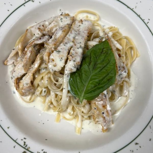 Creamy fettuccine alfredo with sliced chicken and a fresh basil leaf in a white bowl.